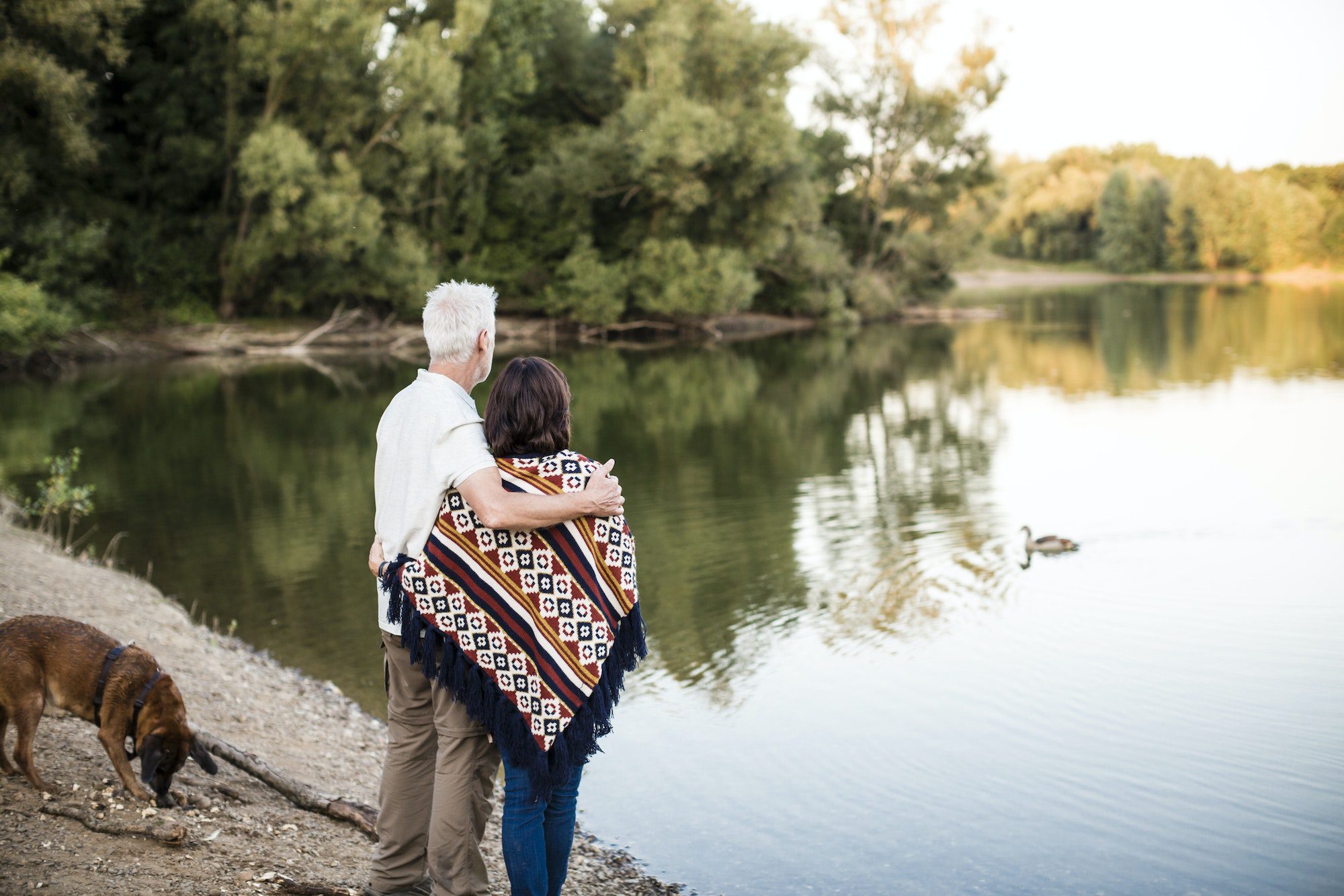 Senior couple with dog at a lake avoid Medicare Penalties