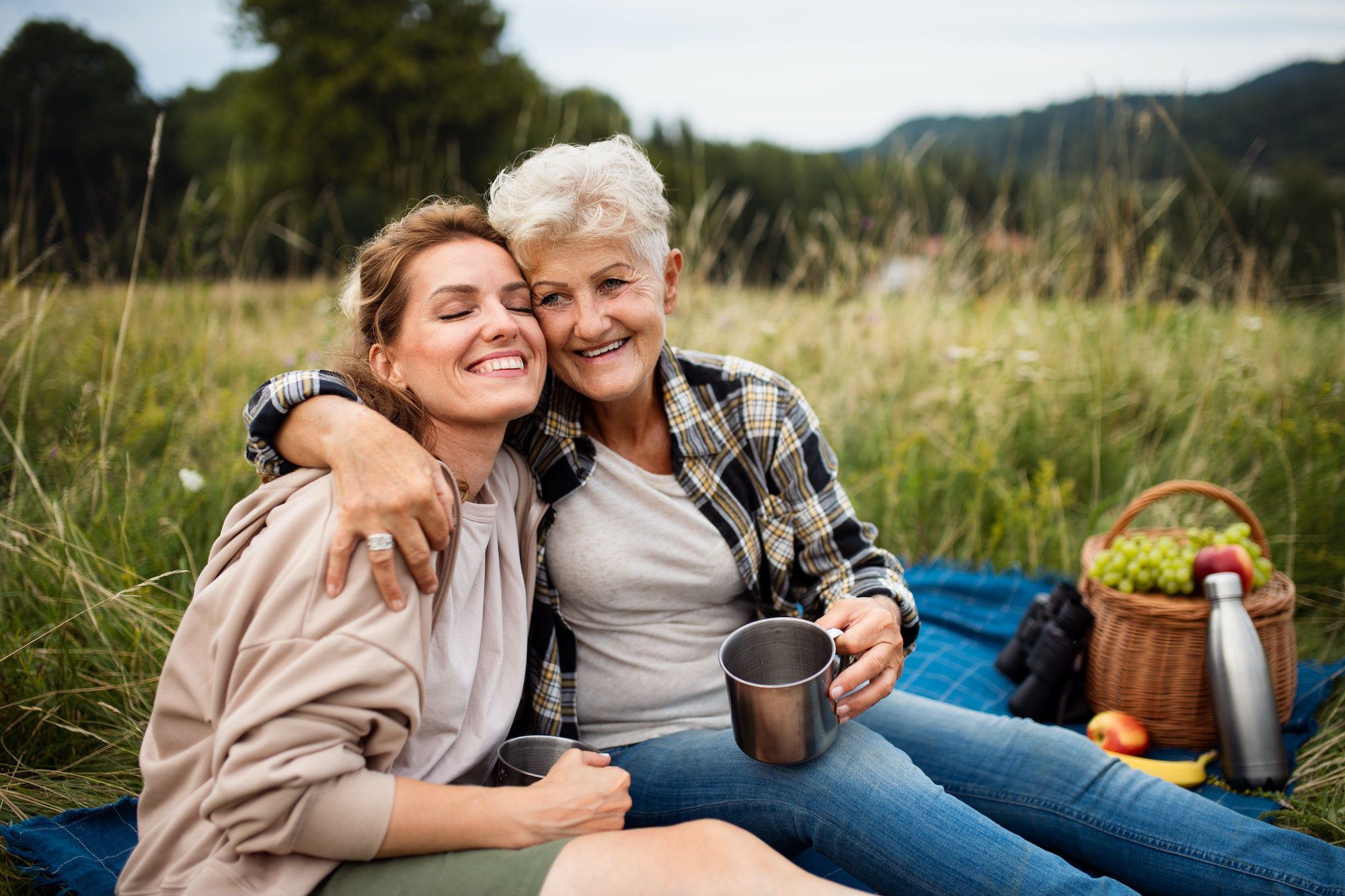 Happy senior mother embracing adult daughter when sitting and having picnic outdoors in nature with Medigap Plan