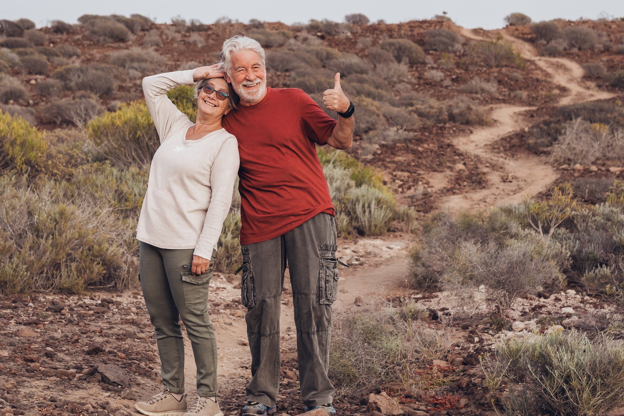 Joyful adult mature senior couple in countryside footpath makes ok gesture with hands and smiles during AEP